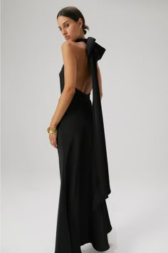 MISHA Evianna Satin Gown in Black. A show-stopping gown for a special someone on their special day. The Evianna Satin maxi dress exudes modern femininity, showcasing high neck and statement back bow detail. - Bias cut skirt- Ruched neckline with buttons at back- Silicone tape around neckline and armholes- Detachable bow and tie- Low scoop back- Invisible centre back zipper Fabric Composition: 100% Polyester Modern Black Bridesmaid Dresses, Black Bridesmaid Dresses Black Tie, Gown With Bow At The Back, Black Black Tie Dress, Formal Wedding Dresses For Guest, Black Bias Cut Dress, Black Tie Black Dress, Black Satin Bridesmaid Dresses, Black Tie Bridesmaid Dresses