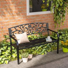 a bench sitting in front of a brick building with potted plants on the side