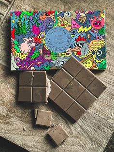 an assortment of chocolates on a wooden table next to a card board with colorful designs