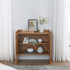 a wooden shelf with books and vases on it in front of a white curtain