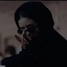 a woman in a black hoodie talking on her cell phone while wearing dark sunglasses