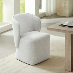 a white chair sitting next to a wooden table in a living room with large windows