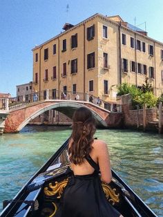 a woman in a black dress riding on the back of a boat down a river