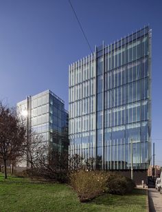 two large glass buildings sitting next to each other on top of a lush green field