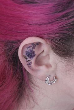 a woman with pink hair has tattoos on her ear and behind the ear is a flower