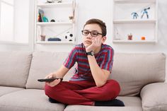 a boy sitting on a couch holding a remote control