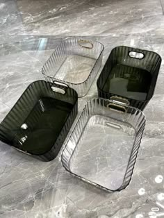 three glass containers sitting on top of a marble counter next to an empty container with handles