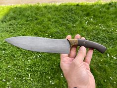 a person holding a knife in their hand on top of green grass with white flowers