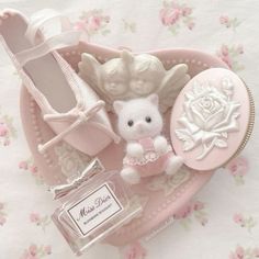 a small white teddy bear sitting on top of a pink heart shaped box next to a perfume bottle