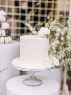 a white wedding cake sitting on top of a table next to other cakes and flowers