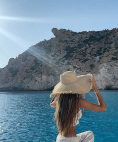 a woman sitting on top of a boat in the ocean wearing a hat and dress