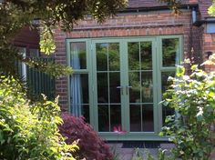 a brick house with green double doors and windows in the front yard, surrounded by greenery