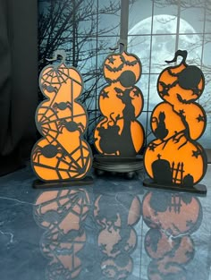 three halloween decorations are sitting on the counter in front of a window with black and orange silhouettes