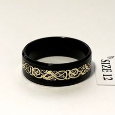 a black and gold ring sitting on top of a white table next to a tag