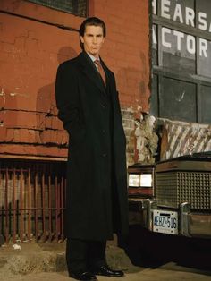 a man standing next to a car in front of a brick building with an advertisement on it