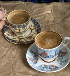 two coffee cups with saucers sitting on top of a table next to each other