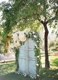 an old door is decorated with white flowers and greenery for a wedding ceremony in the garden