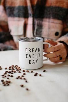 a person holding a coffee mug with the words dream every day printed on it, surrounded by coffee beans