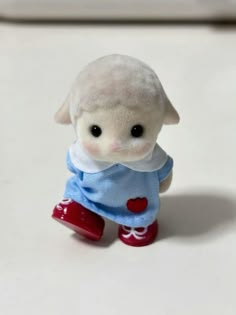 a small white stuffed animal wearing a blue shirt and red boots with hearts on it's chest