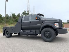 a large gray truck parked in a parking lot next to a light pole and trees