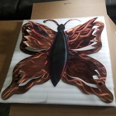 a large metal butterfly sitting on top of a cardboard box with flames all over it