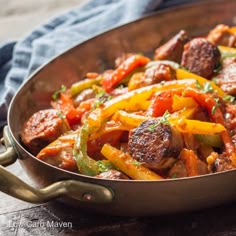 a pan filled with meat and vegetables on top of a wooden table next to a blue towel