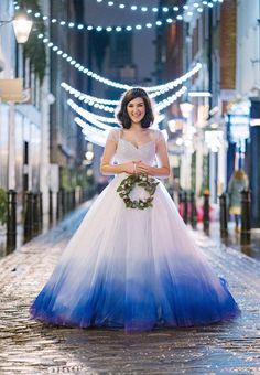 a woman in a blue and white dress is standing on the street with lights behind her