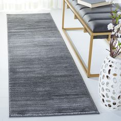 a large gray rug on the floor next to a bench and vase with flowers in it