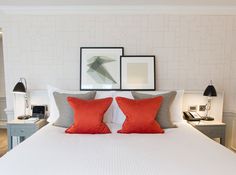 a white bed with red pillows and two framed pictures on the wall above it's headboard