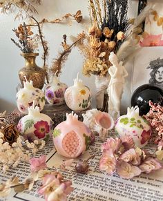 an assortment of decorative vases and flowers on a table with pictures in the background