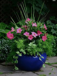 a blue vase filled with pink flowers on top of a stone floor next to greenery