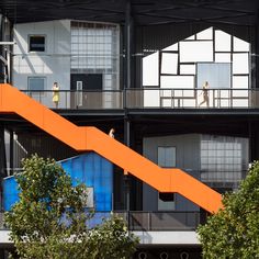 an orange staircase going up the side of a building with two people walking on it