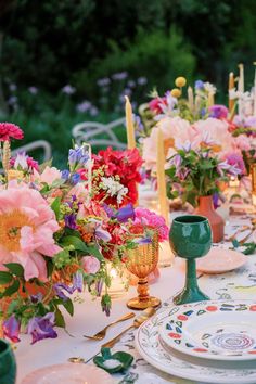 the table is set with colorful flowers, candles and china plates for dinner guests to enjoy