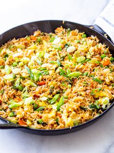 a skillet filled with rice and vegetables on top of a white countertop next to a towel