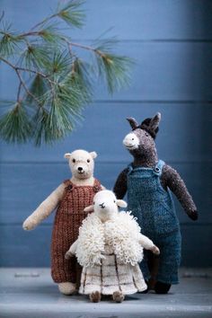 three stuffed animals standing next to each other near a pine tree and blue wall in the background