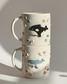 two coffee mugs sitting side by side on top of each other with different sea animals painted on them