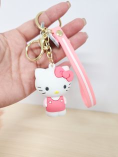 a hand holding a hello kitty keychain with a pink ribbon around it's neck