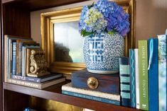 some books and flowers are sitting on a book shelf in front of a framed picture