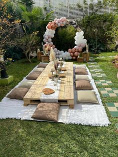 a table with pillows and balloons on it in the middle of a yard area for an outdoor party