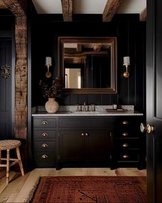 a bathroom with black walls and wooden floors, an area rug and a large mirror on the wall