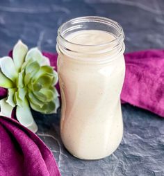 a glass jar filled with white liquid next to a purple cloth and succulent