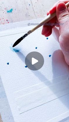 a person is holding a paintbrush and drawing something on paper with watercolors