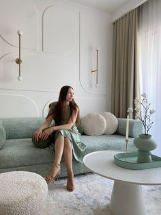 a woman sitting on top of a couch in a living room next to a table