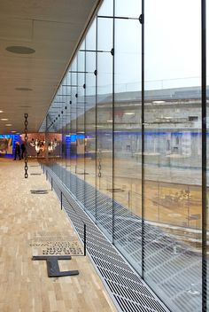 an empty train station with people walking on the platform and in the background, there is a large glass wall