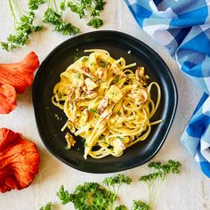 a black plate topped with pasta and parsley on top of a white tablecloth