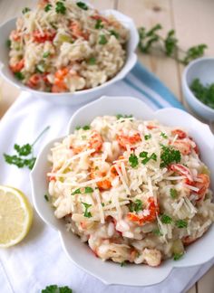 two white bowls filled with pasta and garnished with parmesan cheese next to lemon wedges