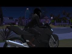 a person riding on the back of a black motorcycle at night with palm trees in the background