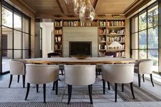 a dining room table surrounded by chairs and bookshelves in front of a fireplace