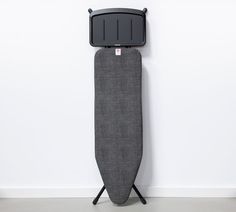 an ironing board on a stand against a white wall with a black cover over it