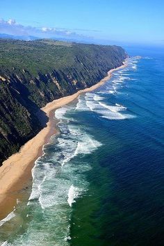 an aerial view of the ocean and beach near a cliff face with waves crashing on it